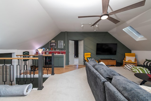 living room featuring ceiling fan, vaulted ceiling with skylight, light hardwood / wood-style flooring, and rail lighting