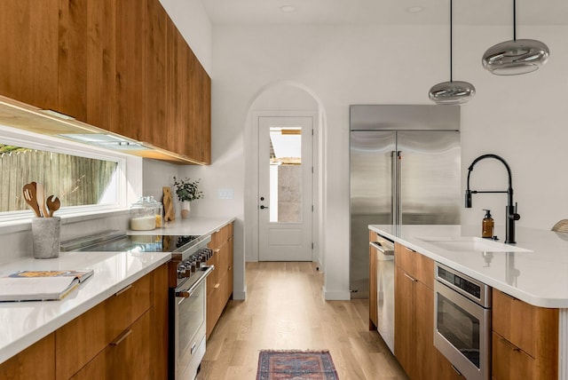 kitchen with pendant lighting, sink, high end appliances, and light hardwood / wood-style floors