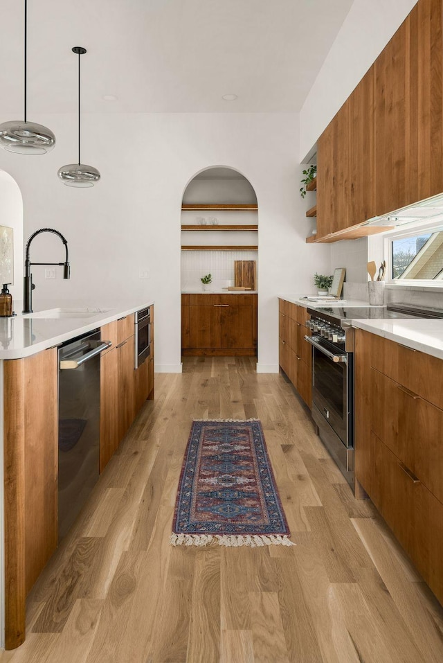 kitchen with appliances with stainless steel finishes, sink, hanging light fixtures, and light wood-type flooring