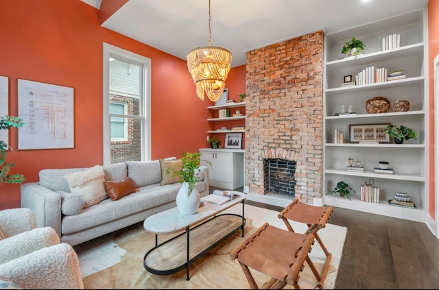 living room with built in shelves, wood-type flooring, a brick fireplace, and a notable chandelier