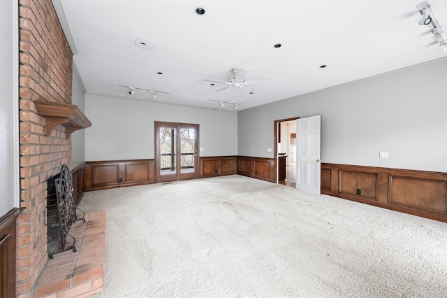 unfurnished living room with ceiling fan, rail lighting, light colored carpet, and a fireplace