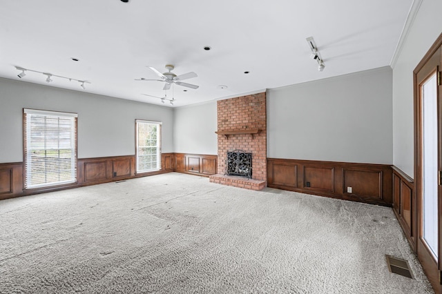 unfurnished living room with a fireplace, carpet floors, ornamental molding, ceiling fan, and track lighting