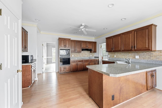 kitchen with sink, kitchen peninsula, black appliances, and light hardwood / wood-style flooring