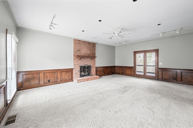 unfurnished living room featuring light carpet, track lighting, crown molding, and a brick fireplace