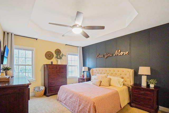 bedroom with multiple windows, light carpet, a raised ceiling, and ceiling fan