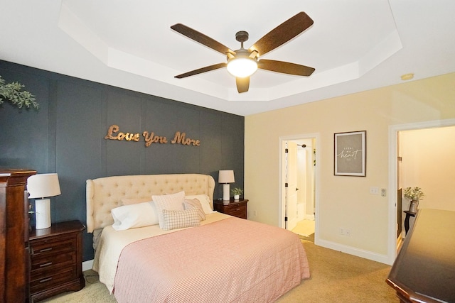 carpeted bedroom with a raised ceiling, connected bathroom, and ceiling fan