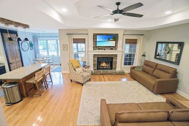 living room with ceiling fan, light hardwood / wood-style flooring, a fireplace, and a tray ceiling