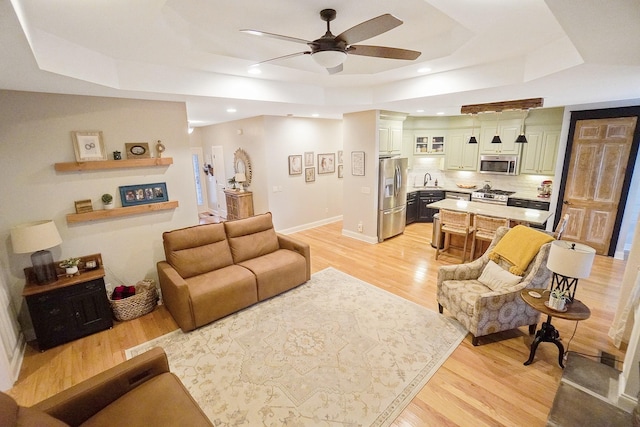 living room with sink, light hardwood / wood-style flooring, a raised ceiling, and ceiling fan