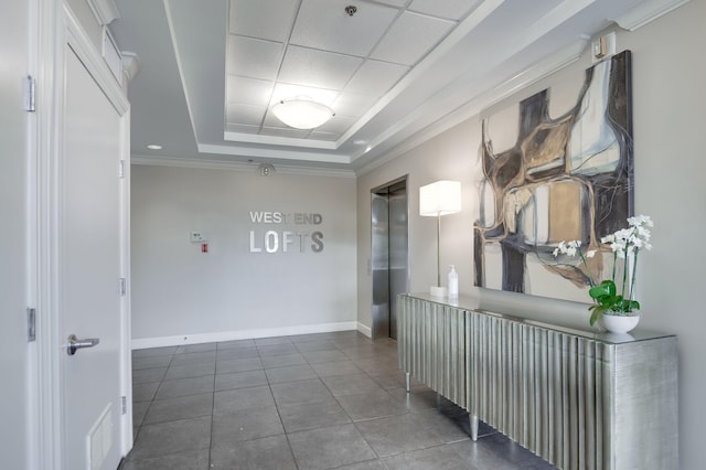 corridor featuring elevator, a paneled ceiling, dark tile patterned floors, ornamental molding, and a tray ceiling