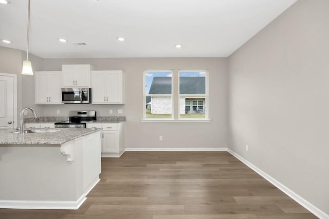 kitchen with appliances with stainless steel finishes, white cabinetry, sink, hanging light fixtures, and light stone countertops