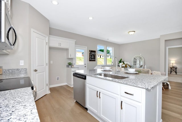 kitchen with appliances with stainless steel finishes, white cabinetry, sink, a kitchen island with sink, and light stone counters