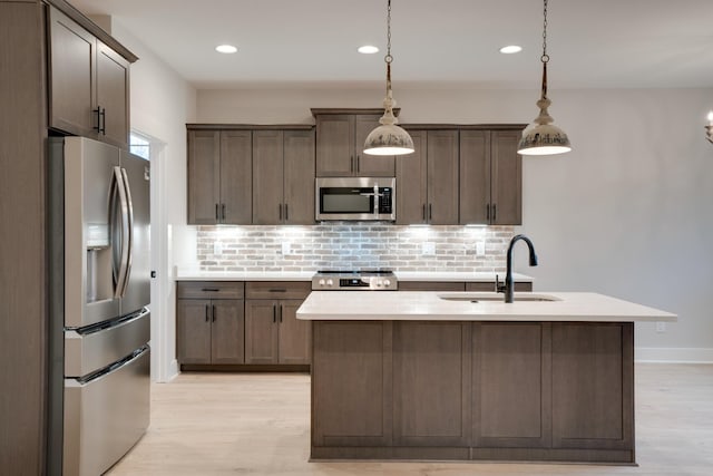 kitchen with sink, tasteful backsplash, appliances with stainless steel finishes, an island with sink, and pendant lighting