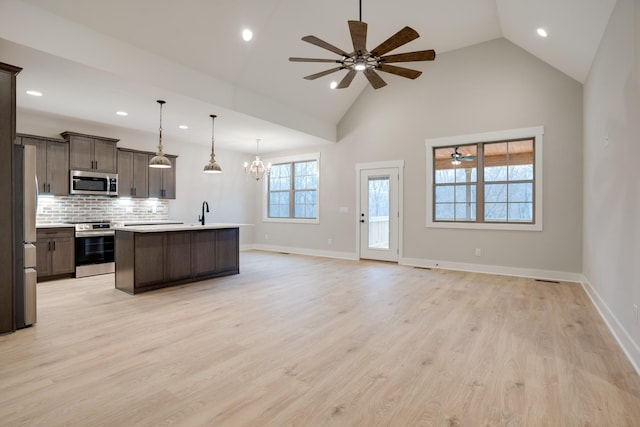 kitchen featuring appliances with stainless steel finishes, decorative light fixtures, an island with sink, dark brown cabinets, and light wood-type flooring