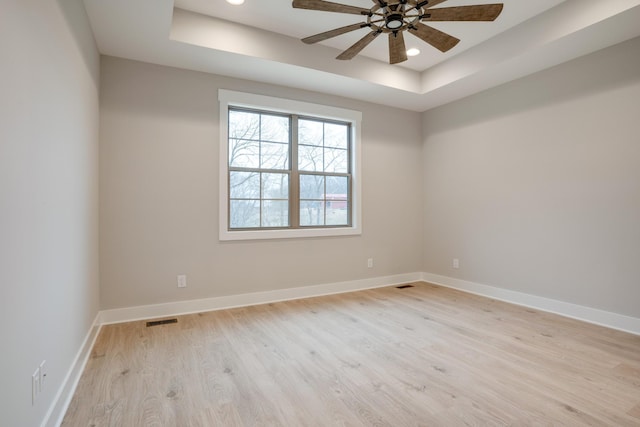 spare room featuring a tray ceiling, ceiling fan, and light hardwood / wood-style flooring