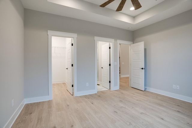 unfurnished bedroom featuring ceiling fan, a walk in closet, a tray ceiling, and light hardwood / wood-style floors