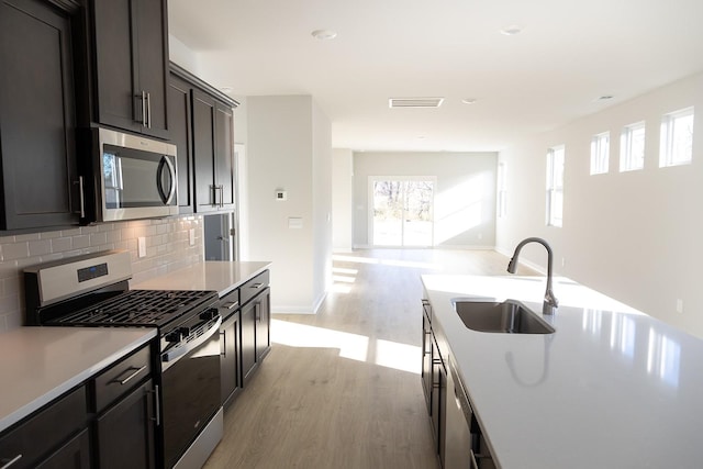 kitchen with stainless steel appliances, sink, decorative backsplash, and light hardwood / wood-style flooring