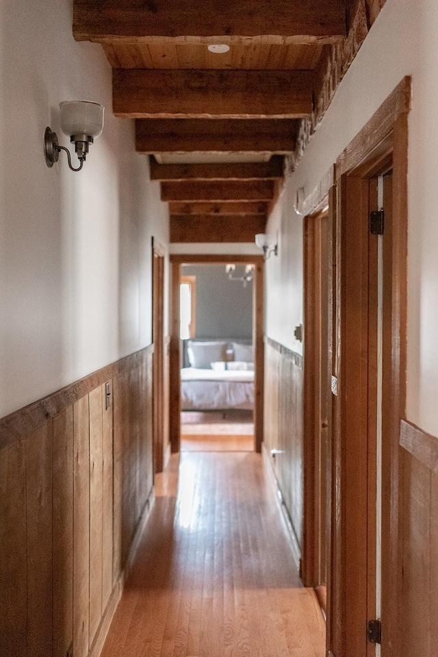 hall with wooden walls, wooden ceiling, beam ceiling, and light hardwood / wood-style flooring