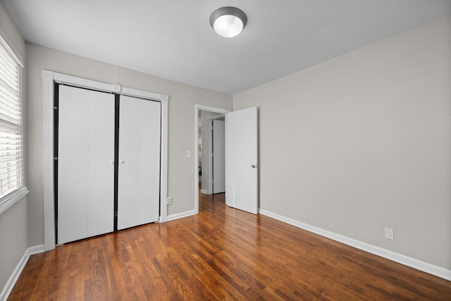 unfurnished bedroom with multiple windows, dark wood-type flooring, and a closet