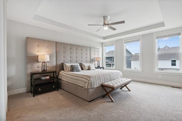 carpeted bedroom featuring ceiling fan and a tray ceiling