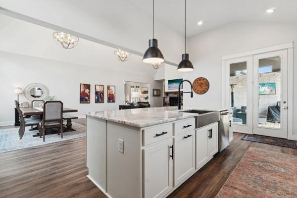 kitchen with decorative light fixtures, white cabinetry, sink, a kitchen island with sink, and light stone countertops