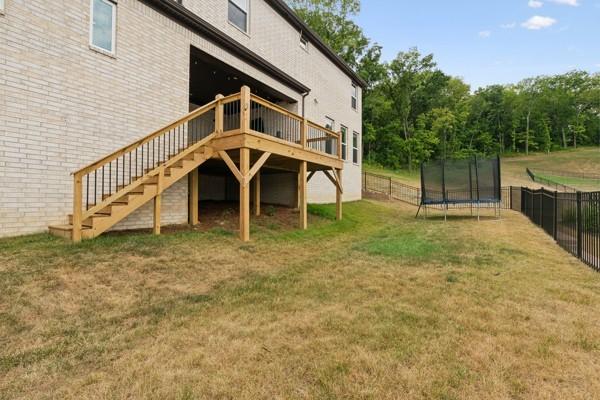 rear view of property with a trampoline, a lawn, and a deck