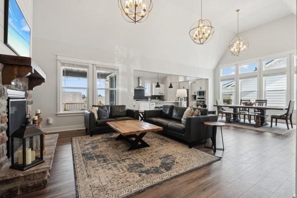 living room with dark hardwood / wood-style floors, high vaulted ceiling, a stone fireplace, and a notable chandelier