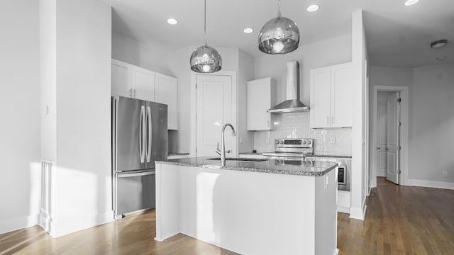 kitchen featuring wall chimney exhaust hood, sink, white cabinetry, stainless steel appliances, and a kitchen island with sink