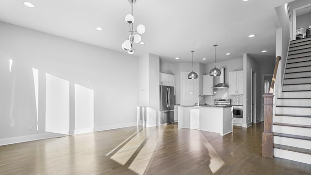 kitchen with sink, stainless steel refrigerator, a kitchen island with sink, white cabinets, and decorative light fixtures