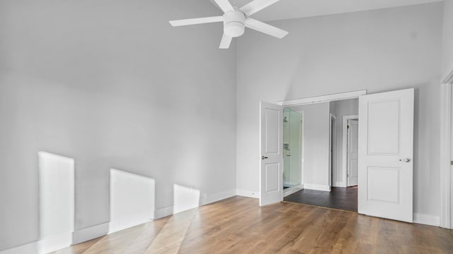 unfurnished bedroom featuring hardwood / wood-style flooring, ceiling fan, and a high ceiling