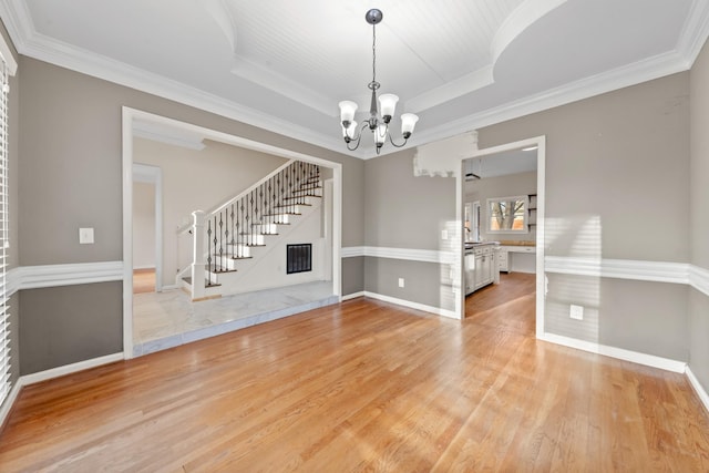 interior space featuring crown molding, an inviting chandelier, light wood-type flooring, and a tray ceiling