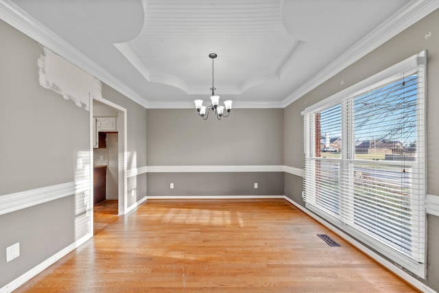 unfurnished dining area featuring crown molding, a raised ceiling, hardwood / wood-style floors, and a notable chandelier