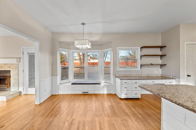 unfurnished dining area featuring a stone fireplace, plenty of natural light, and light wood-type flooring