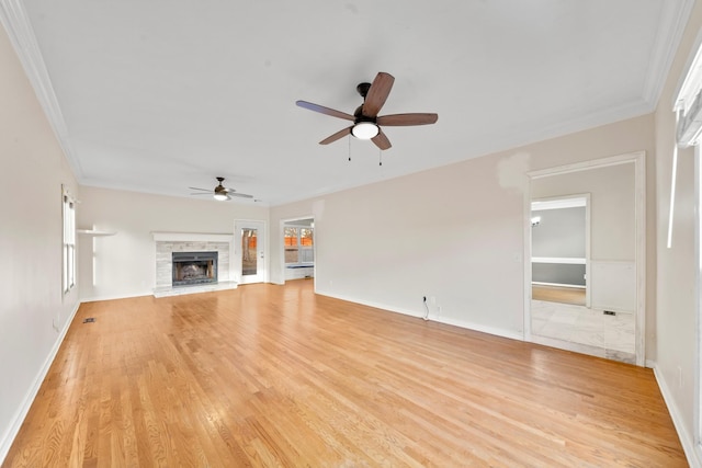 unfurnished living room featuring crown molding, a stone fireplace, ceiling fan, and light hardwood / wood-style floors