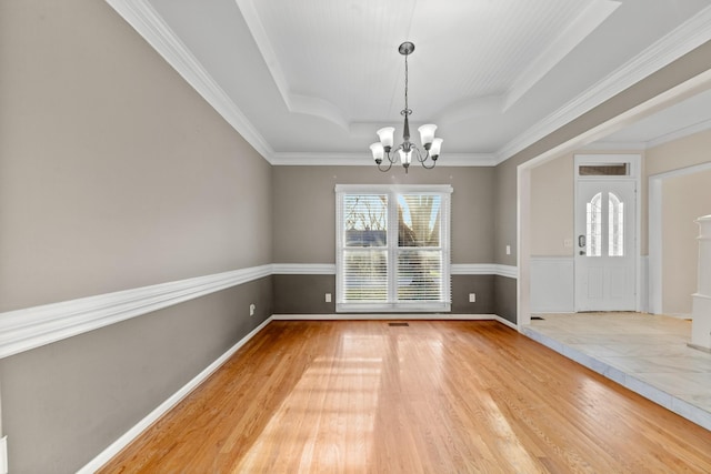 unfurnished dining area with hardwood / wood-style floors, a notable chandelier, ornamental molding, and a raised ceiling