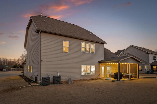 back house at dusk featuring a sunroom and central air condition unit