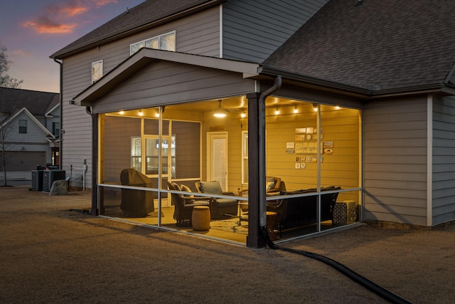 back house at dusk with a sunroom and central AC unit