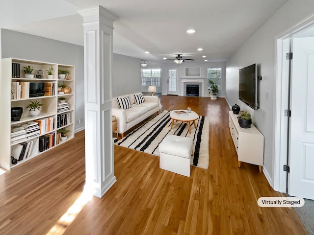 living room featuring light wood-type flooring, ceiling fan, and ornate columns