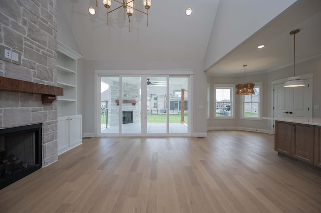 unfurnished living room with built in shelves, a stone fireplace, high vaulted ceiling, and light hardwood / wood-style flooring