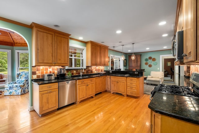 kitchen featuring appliances with stainless steel finishes, decorative light fixtures, sink, kitchen peninsula, and light wood-type flooring