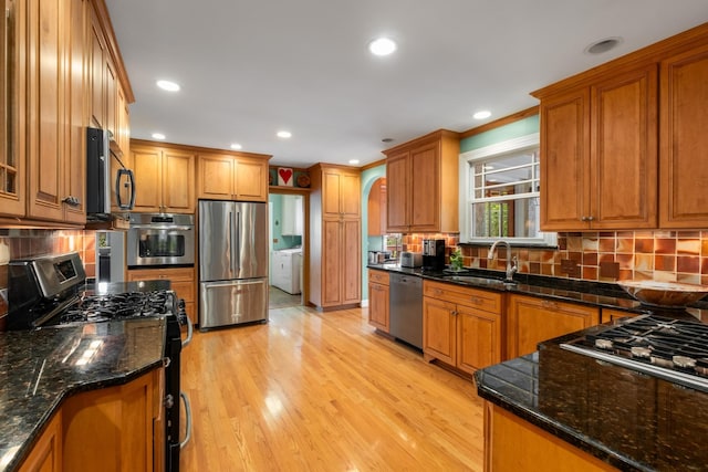 kitchen featuring sink, dark stone countertops, stainless steel appliances, light hardwood / wood-style floors, and washer / dryer