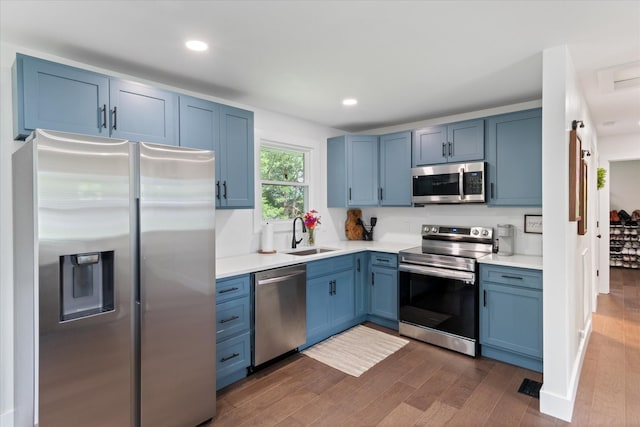 kitchen with sink, blue cabinetry, appliances with stainless steel finishes, dark hardwood / wood-style flooring, and a barn door