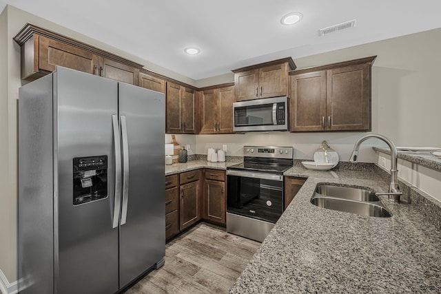 kitchen featuring stainless steel appliances, light hardwood / wood-style floors, sink, and stone counters