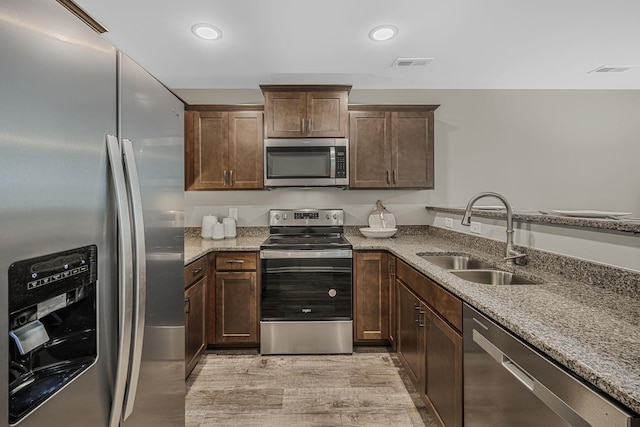 kitchen with sink, dark brown cabinets, stainless steel appliances, light hardwood / wood-style floors, and light stone countertops