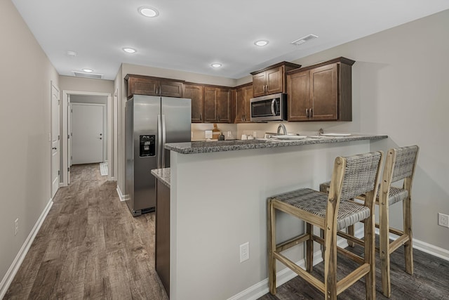 kitchen with appliances with stainless steel finishes, dark stone counters, dark brown cabinetry, and kitchen peninsula