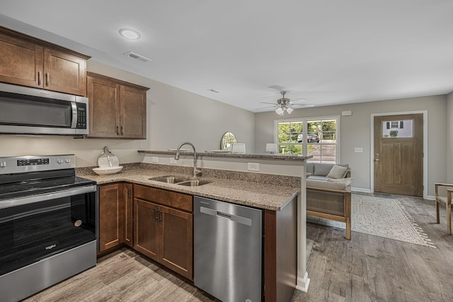 kitchen with sink, light stone counters, kitchen peninsula, stainless steel appliances, and light hardwood / wood-style floors