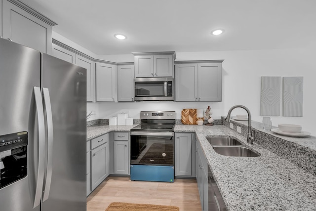 kitchen with sink, appliances with stainless steel finishes, gray cabinetry, light stone counters, and light wood-type flooring