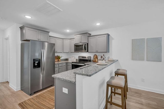 kitchen with appliances with stainless steel finishes, a kitchen breakfast bar, light stone counters, kitchen peninsula, and light wood-type flooring