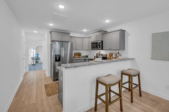 kitchen with gray cabinets, appliances with stainless steel finishes, light hardwood / wood-style floors, and kitchen peninsula