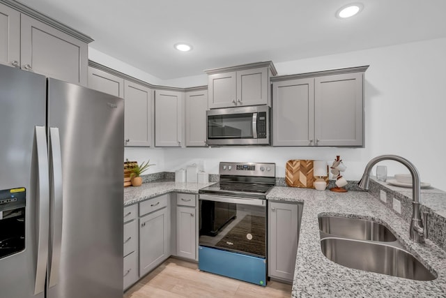 kitchen with sink, appliances with stainless steel finishes, gray cabinetry, light stone counters, and light hardwood / wood-style floors