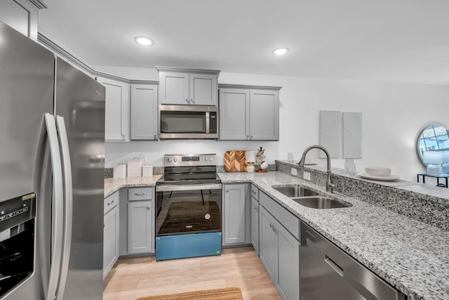 kitchen featuring sink, gray cabinetry, light wood-type flooring, appliances with stainless steel finishes, and light stone countertops